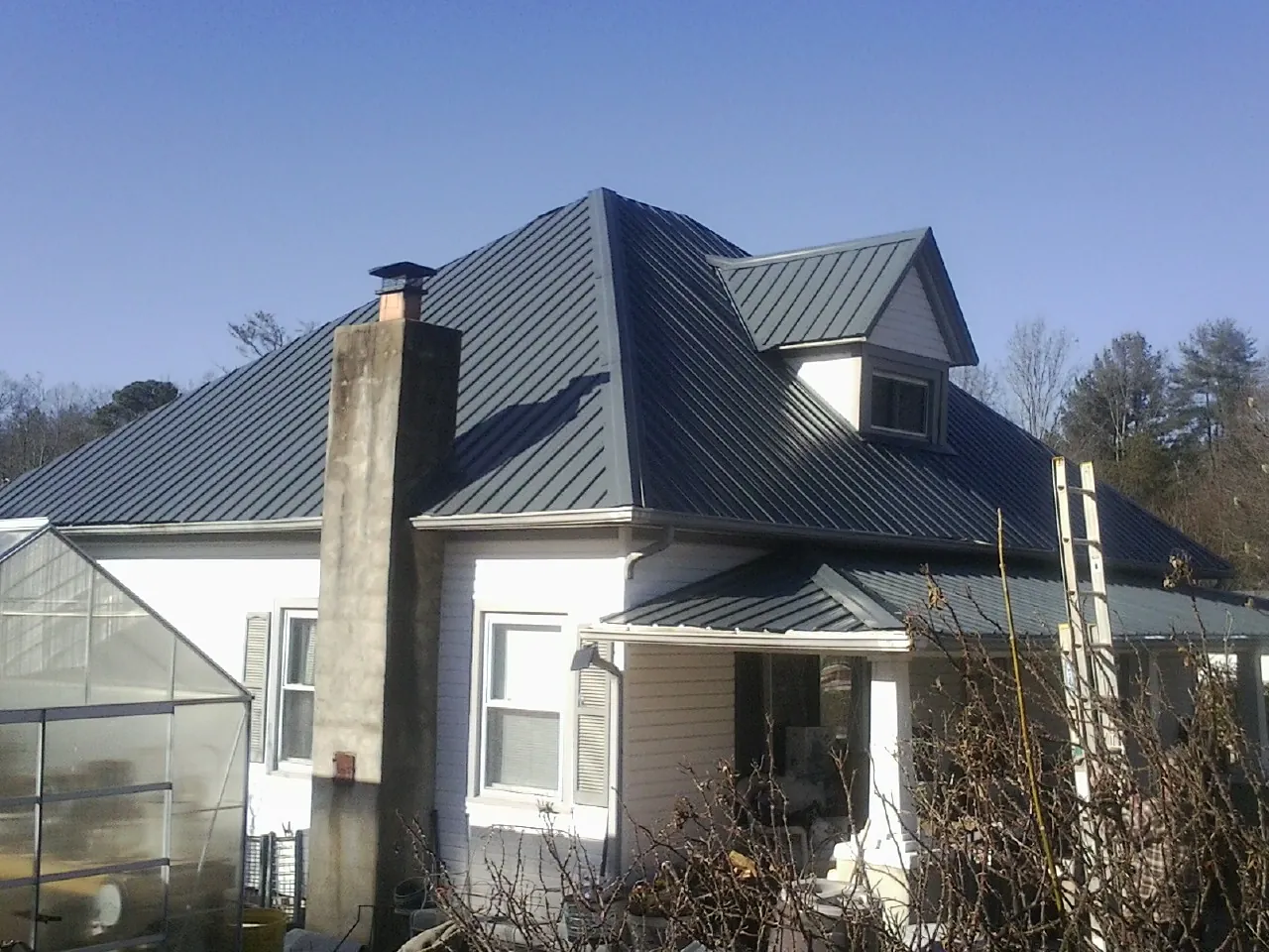 Dark blue standing seam metal roof on a white farmhouse with dormer in Camillus