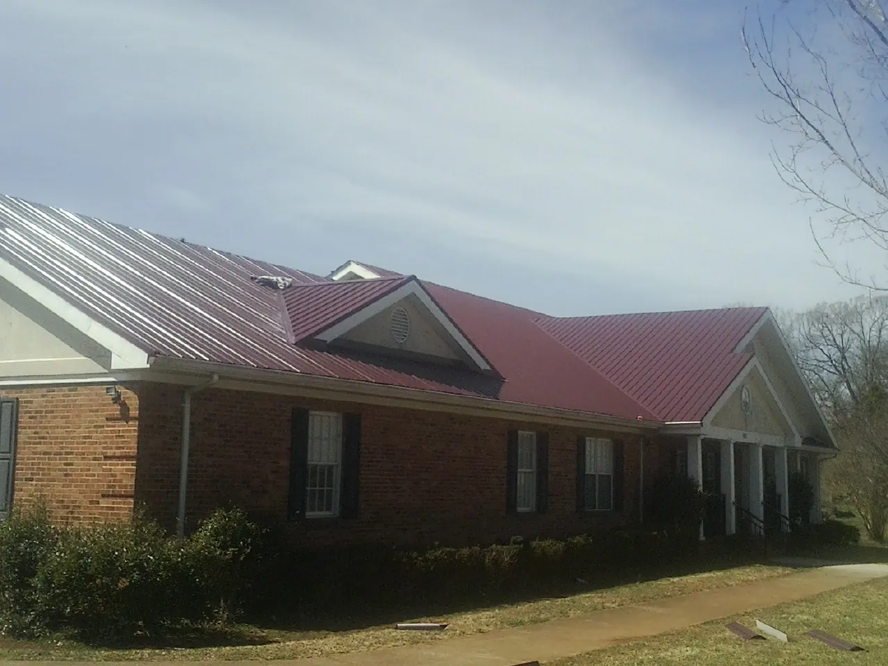 Red metal roof with gabled entries on a long brick building, from a Hail Damage Roof Repair job in Camillus