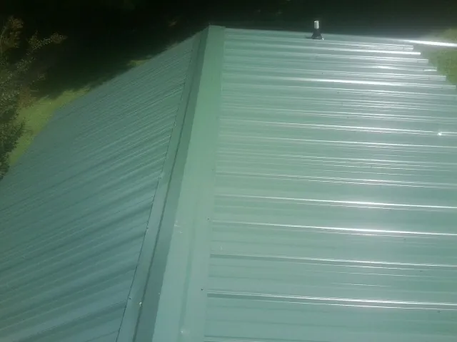 New green metal panels meeting at the ridge of a roof — Flat Roof Repair work by our crew in Camillus