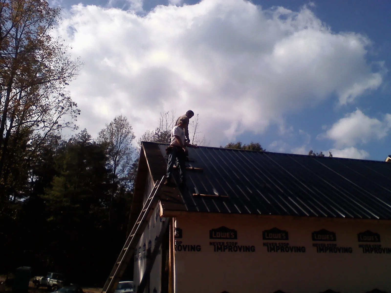 Roofer fastening dark metal panels high against a cloudy sky, from a Roof Inspection job in Camillus